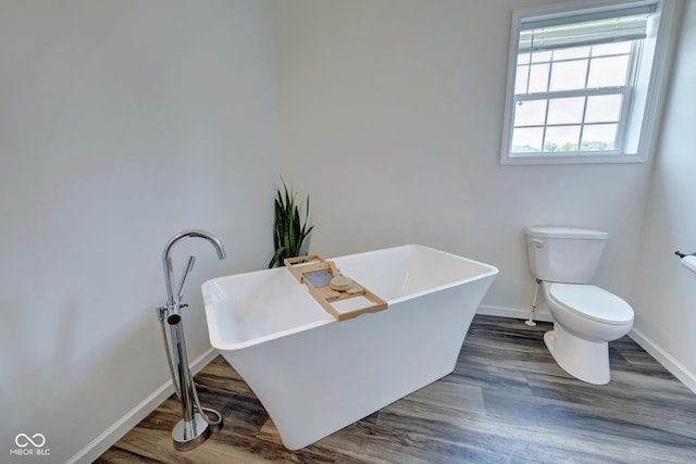 bathroom featuring baseboards, a freestanding bath, toilet, and wood finished floors