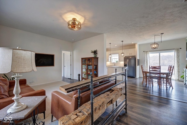 living area featuring a chandelier, dark wood-type flooring, a textured ceiling, and baseboards