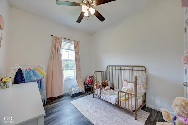 bedroom with a crib, a ceiling fan, baseboards, and wood finished floors