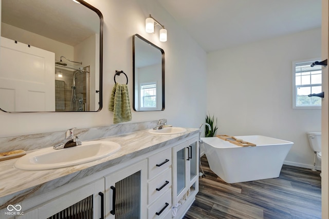 bathroom featuring double vanity, wood finished floors, a sink, and tiled shower