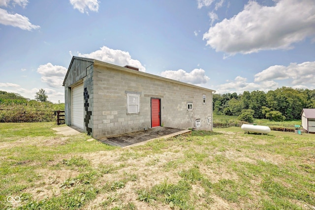 rear view of house featuring a detached garage, concrete block siding, fence, and a yard