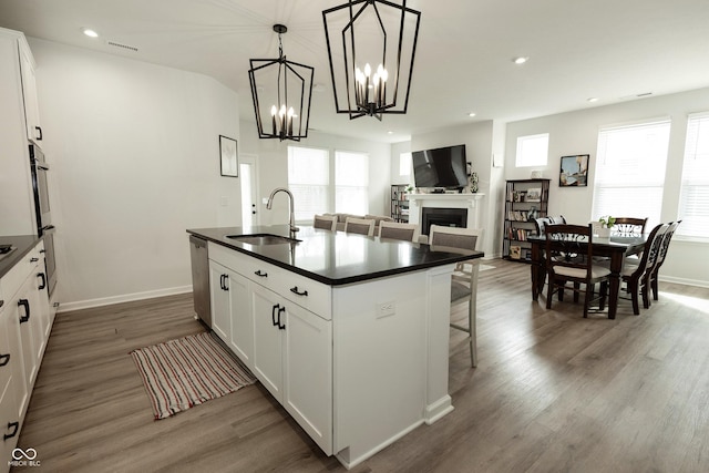 kitchen featuring dark countertops, wood finished floors, a sink, a fireplace, and stainless steel dishwasher