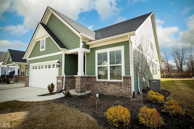 craftsman-style home with brick siding, a shingled roof, cooling unit, concrete driveway, and an attached garage