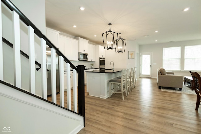 kitchen featuring light wood-style flooring, stainless steel appliances, a sink, white cabinetry, and dark countertops