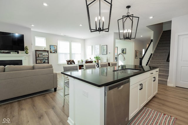 kitchen featuring dark countertops, open floor plan, wood finished floors, stainless steel dishwasher, and a sink