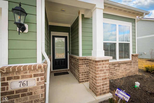 entrance to property featuring a porch and brick siding