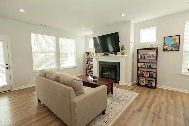 living room with recessed lighting, visible vents, light wood-style flooring, a glass covered fireplace, and baseboards