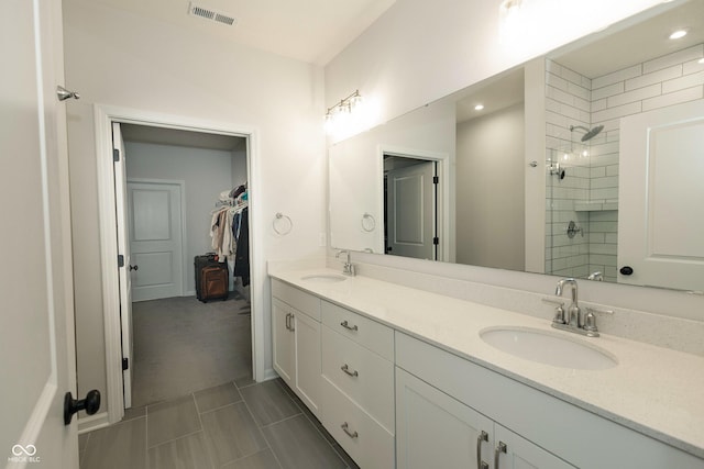 bathroom with double vanity, visible vents, a sink, and tiled shower