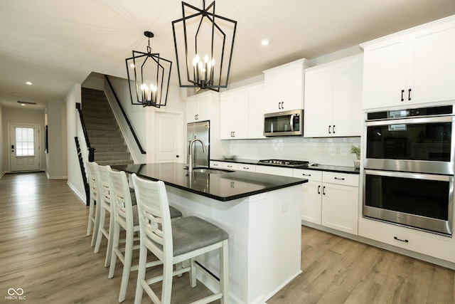 kitchen with dark countertops, a center island with sink, stainless steel appliances, and a sink