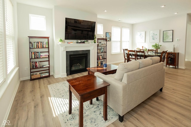 living area with baseboards, a glass covered fireplace, light wood-style flooring, and recessed lighting