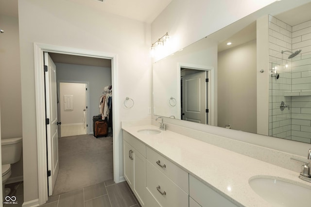 full bathroom with toilet, double vanity, a sink, and tiled shower