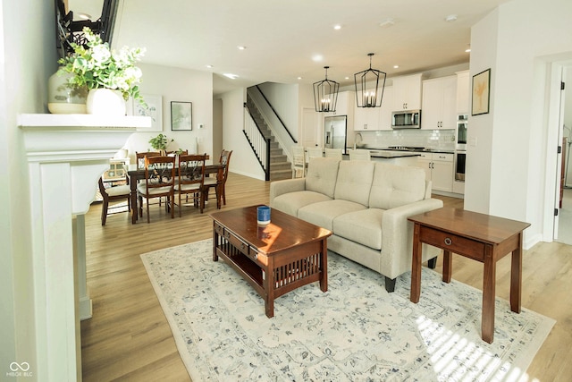 living area featuring a chandelier, recessed lighting, baseboards, stairway, and light wood finished floors