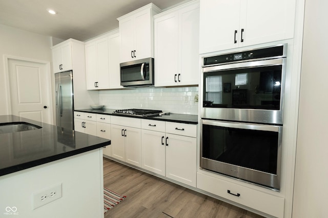 kitchen with stainless steel appliances, tasteful backsplash, dark countertops, and light wood-style floors