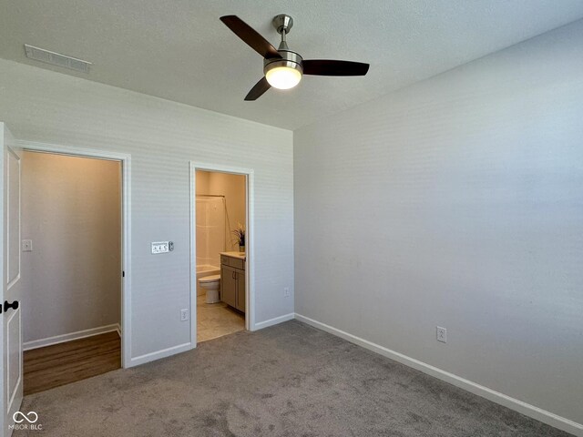 unfurnished bedroom featuring light colored carpet, ceiling fan, ensuite bathroom, baseboards, and visible vents