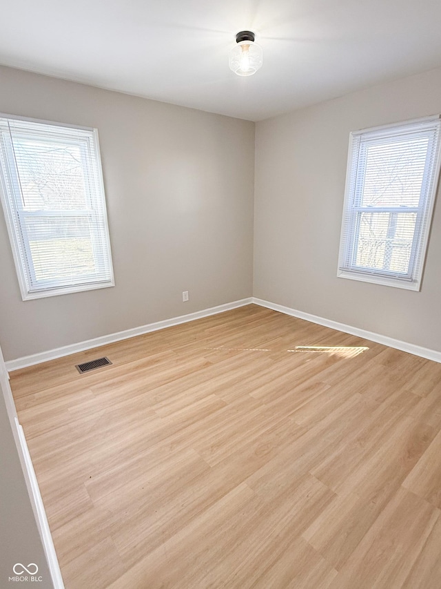 unfurnished room featuring visible vents, light wood-style flooring, and baseboards