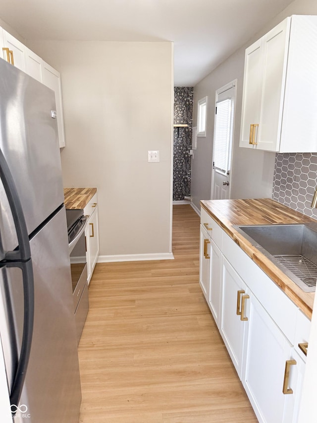 kitchen with light wood finished floors, butcher block counters, appliances with stainless steel finishes, white cabinetry, and a sink