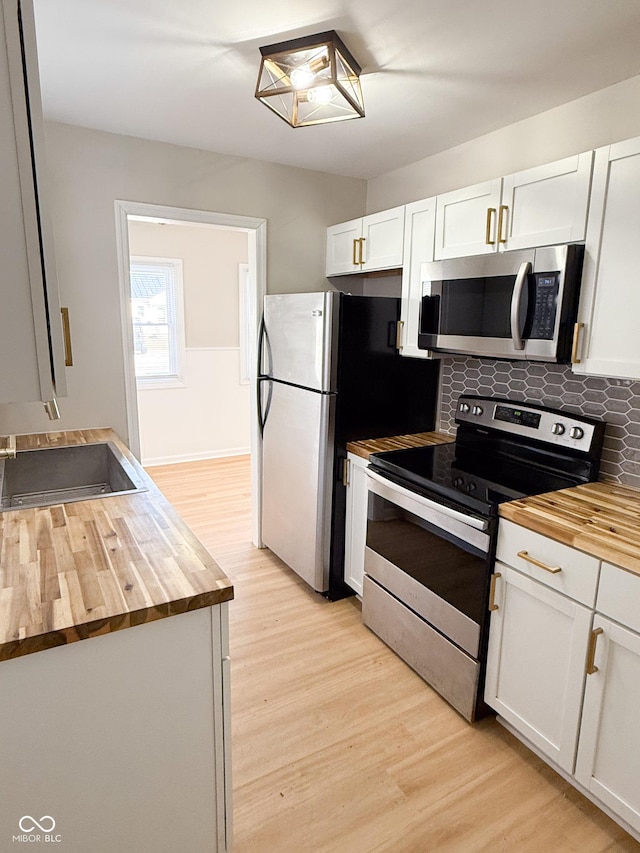 kitchen featuring tasteful backsplash, light wood-style flooring, appliances with stainless steel finishes, white cabinets, and butcher block countertops