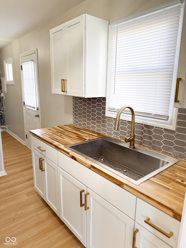 kitchen featuring butcher block countertops, light wood-type flooring, white cabinetry, and a sink