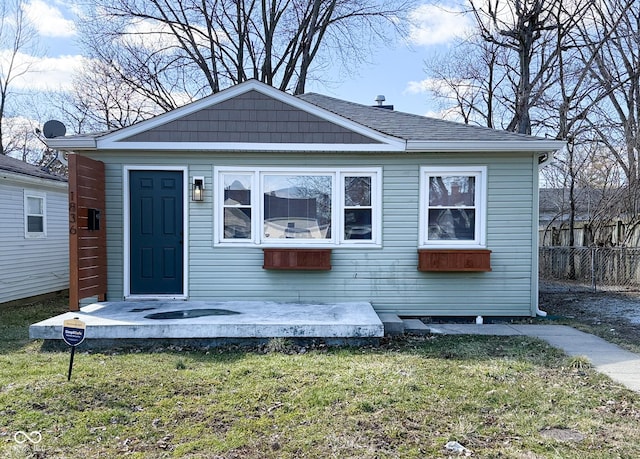 bungalow-style home featuring roof with shingles, fence, and a front lawn