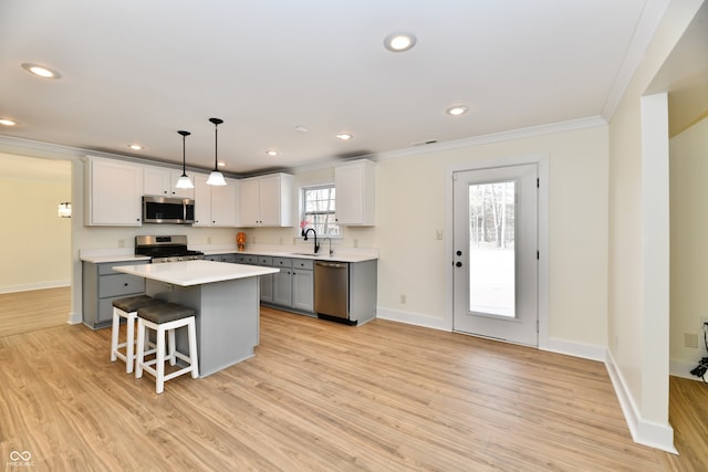 kitchen with light wood finished floors, crown molding, light countertops, stainless steel appliances, and a sink