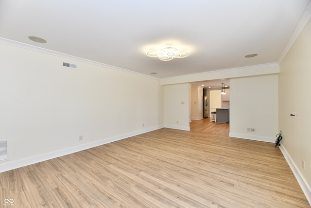 empty room with visible vents, light wood-type flooring, crown molding, and baseboards