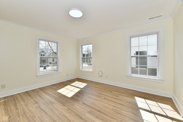 spare room with light wood-type flooring, baseboards, visible vents, and ornamental molding