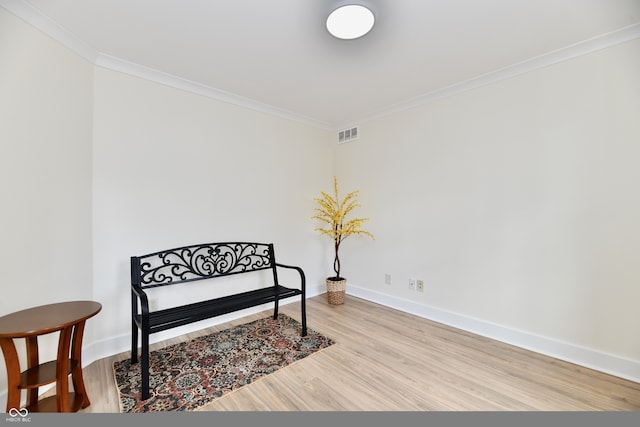 living area with visible vents, baseboards, light wood-style flooring, and crown molding