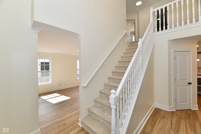 stairs with crown molding, wood finished floors, baseboards, and a towering ceiling