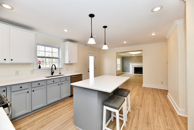 kitchen featuring gray cabinetry, a center island, light wood-style flooring, a fireplace, and a sink