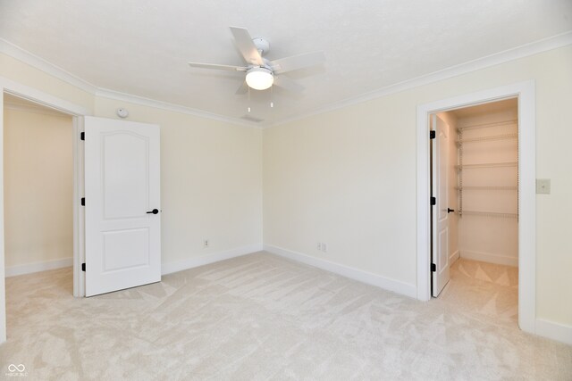 unfurnished bedroom featuring a walk in closet, crown molding, light colored carpet, and baseboards