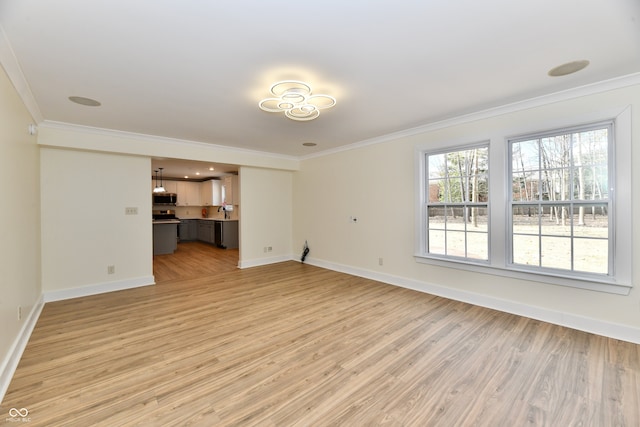 unfurnished living room featuring a sink, baseboards, ornamental molding, and light wood finished floors