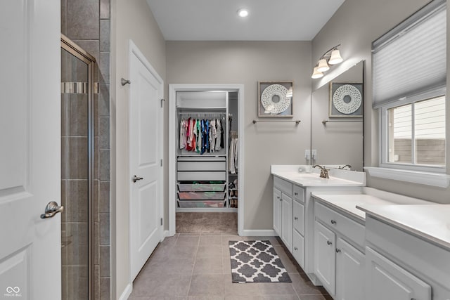 bathroom with a walk in closet, a tile shower, vanity, tile patterned flooring, and baseboards