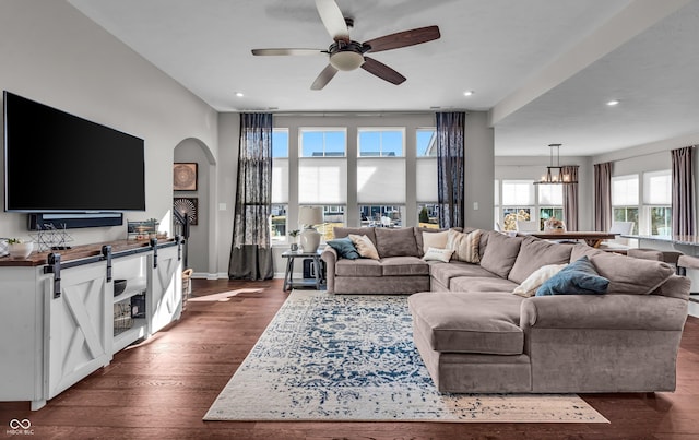 living room featuring baseboards, arched walkways, dark wood-style floors, ceiling fan with notable chandelier, and recessed lighting