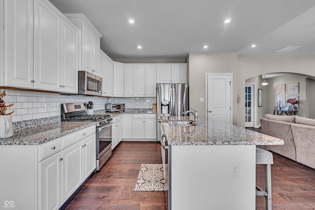 kitchen featuring arched walkways, a breakfast bar area, open floor plan, dark wood-type flooring, and stainless steel appliances