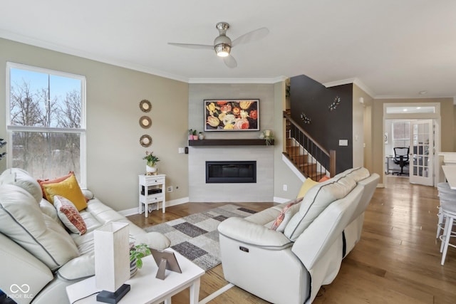 living area featuring crown molding, baseboards, wood finished floors, a glass covered fireplace, and a ceiling fan