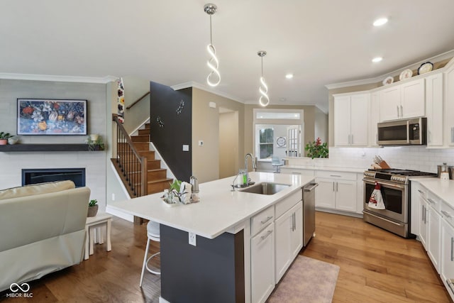 kitchen with ornamental molding, light wood-style flooring, a glass covered fireplace, stainless steel appliances, and a sink