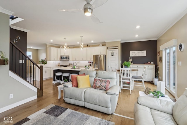 living area featuring crown molding, baseboards, light wood-type flooring, stairs, and recessed lighting