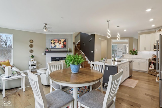 dining space featuring a glass covered fireplace, stairs, light wood-style floors, and ornamental molding