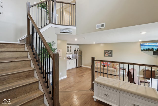 stairway with wood finished floors, visible vents, baseboards, a high ceiling, and recessed lighting