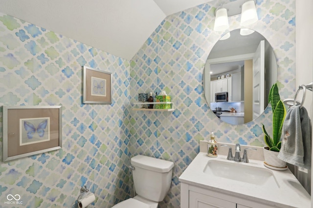 half bathroom with vanity, toilet, and wallpapered walls