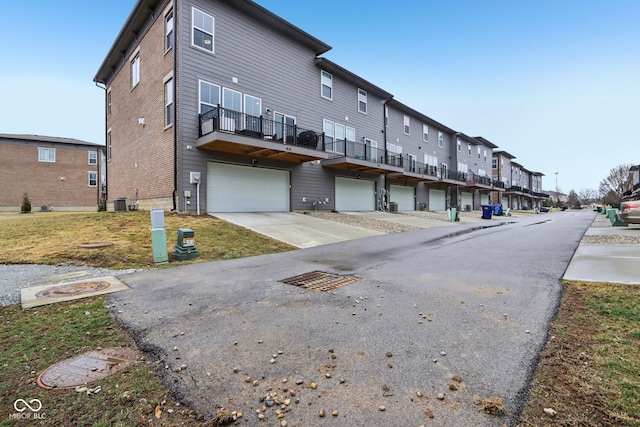 back of house featuring a residential view, cooling unit, an attached garage, and driveway