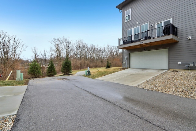 view of side of property featuring aphalt driveway, a balcony, and an attached garage