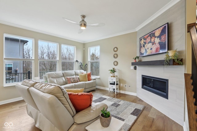 living area featuring a tiled fireplace, crown molding, wood finished floors, and baseboards