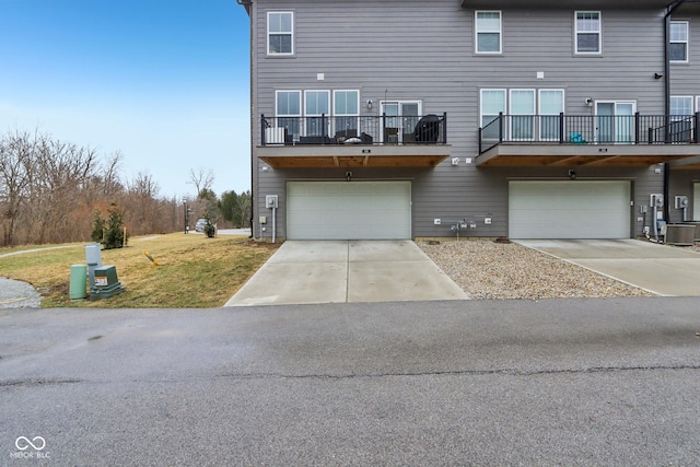 back of property featuring central AC, a lawn, driveway, a balcony, and an attached garage