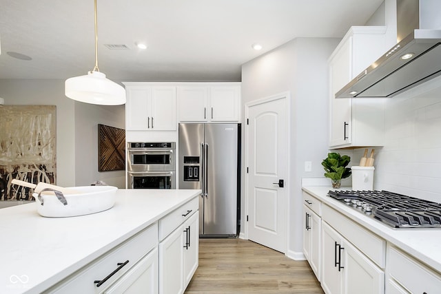 kitchen featuring white cabinetry, appliances with stainless steel finishes, wall chimney exhaust hood, light wood finished floors, and tasteful backsplash