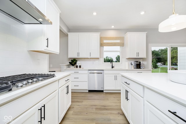 kitchen with a sink, exhaust hood, white cabinets, light wood-type flooring, and tasteful backsplash