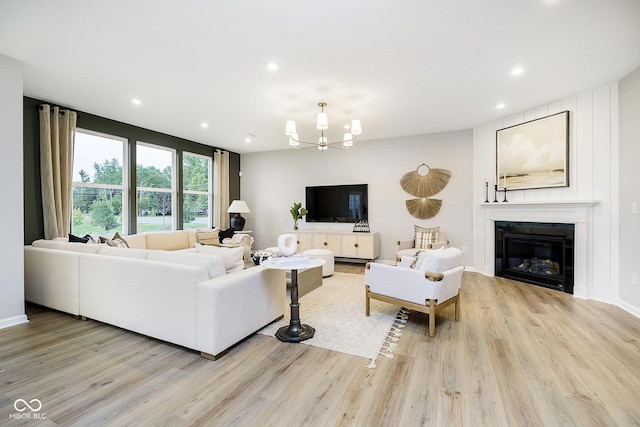 living area with a glass covered fireplace, a notable chandelier, light wood-style flooring, and recessed lighting