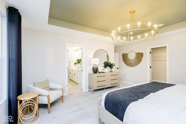 bedroom with a notable chandelier, light colored carpet, baseboards, a tray ceiling, and ensuite bath