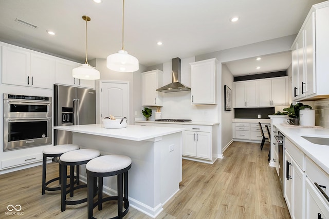 kitchen featuring appliances with stainless steel finishes, light wood-type flooring, wall chimney range hood, a kitchen bar, and backsplash