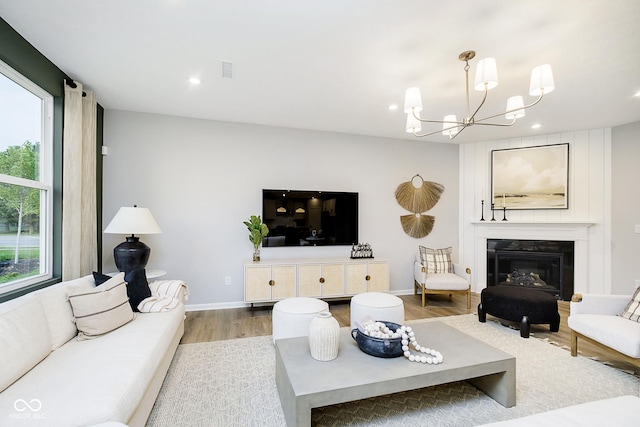 living area with baseboards, visible vents, a glass covered fireplace, wood finished floors, and a notable chandelier